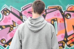 A young graffiti artist in a gray hoodie looks at the wall with photo