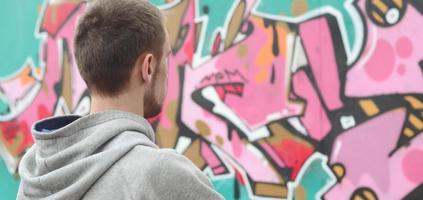 A young graffiti artist in a gray hoodie looks at the wall with photo