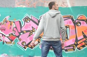 A young graffiti artist in a gray hoodie looks at the wall with photo