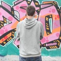 A young graffiti artist in a gray hoodie looks at the wall with photo