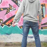 A young graffiti artist in a gray hoodie looks at the wall with photo