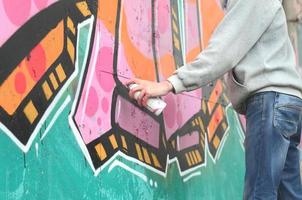 Hand of a young guy in a gray hoodie paints graffiti in pink and photo