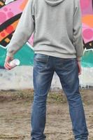 A young graffiti artist in a gray hoodie looks at the wall with photo