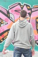 A young graffiti artist in a gray hoodie looks at the wall with photo