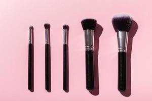 Various make-up brushes on pink background, top view. Cosmetics and beauty concept. photo