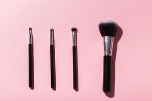 Various make-up brushes on pink background, top view. Cosmetics and beauty concept. photo