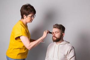 maquillador profesional haciendo maquillaje de hombre joven en estudio foto