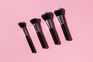 Various make-up brushes on pink background, top view. Cosmetics and beauty concept. photo