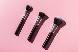 Various make-up brushes on pink background, top view. Cosmetics and beauty concept. photo