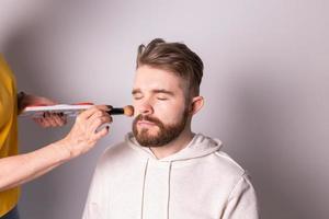 Bearded man getting makeup. Hand of visagist using brush. photo