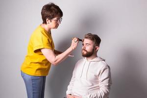 Bearded man getting makeup. Woman visagist works with brush. photo