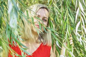 Portrait of a young blonde woman in the foliage of a weeping willow. summer time vacation photo