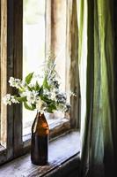 A bottle with blooming jasmine branches by the window in a rustic house photo