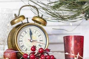 There is an alarm clock with Christmas decorations on the shelf. On the clock five minutes before the new year, Christmas photo