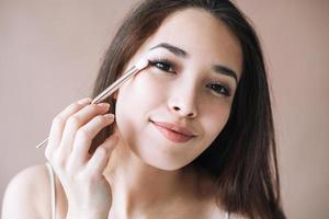 Portrait of young asian woman with makeup brush on beige background photo