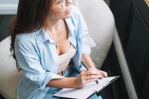 Crop photo of young woman in bue shirt with notes in hands sitting on chair in room