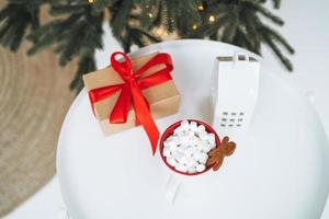 Christmas still life of present gift box, cocoa with marshmallow on white table, top view photo