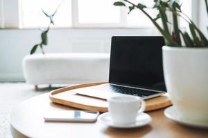 lugar de trabajo con taza de café, computadora portátil abierta en una mesa de madera en la sala de oficina, interior de negocios foto