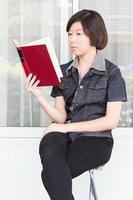 mujer joven leyendo un libro sentado en una silla foto