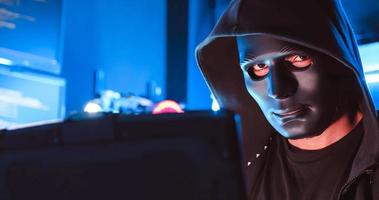 A hacker wearing a mask to cover his face is using computer to hack data to get ransom from victims. photo