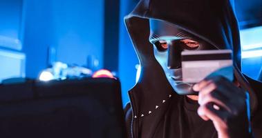 A hacker wearing a mask to cover his face is using computer to hack data to get ransom from victims. photo