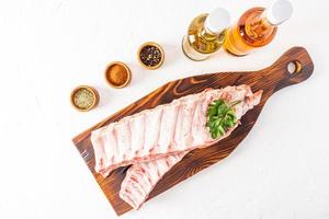 raw farm pork ribs on a wooden dark cutting board surrounded by spices in marinade bowls. white background. photo