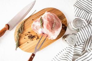 A large piece of pork ham lies on a rosemary cutting board for preparing a menu dish. top view. the process of preparing the cutting of meat. photo