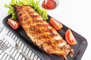 juicy grilled ribs on a ceramic dark tray with tomatoes and lettuce. tomato sauce in a bowl, to improve the taste. close angle. photo