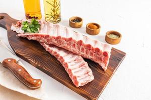 raw juicy pork ribs on a wooden cutting board with various spices in bowls for making a marinade. white background. photo