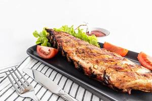 delicious toasted pork ribs on a flat ceramic plate with fresh vegetables. white background. a copy of the space. recipe menu. photo