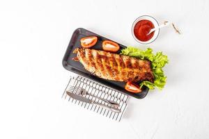 Top view of the delicious, juicy ribs of the barbecue on a ceramic tray with fresh vegetables. grilled pork ribs. sauce in a bowl . space for text. photo