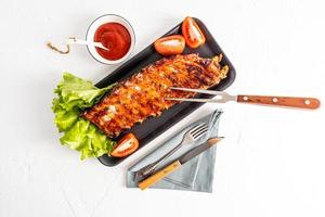 grilled pork ribs on a ceramic rectangular plate with fresh tomato slices and lettuce. sauce to improve the taste. top view. white background. photo