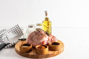 Front view of a large piece of raw pork meat and various spices in marinade bowls on a culinary round board. white background. photo