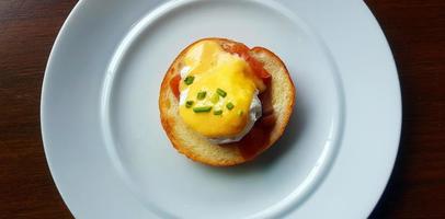 Flat ay of bread with poached egg, bacon and sweet sauce on top in dish. Top view of delicious meal of breakfast on white plate in American style. Close up food on table. photo