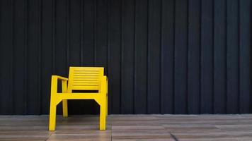 silla de madera amarilla colocada en el suelo de baldosas marrones con una pared de persiana negra para el fondo y espacio para copiar a la derecha. objeto para tomar asiento con papel pintado de acero inoxidable oscuro. foto