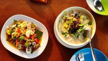 Top view of Thai chicken with coconut soup, spicy seafood salad with fresh vegetable, dish or plate, spoon and fork for dinner. Asian and Famous food concept photo