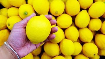 Close up hand of person holding lemon with copy space. Selection and Choice for buy best food, vegetable or fruit at market or supermarket. photo