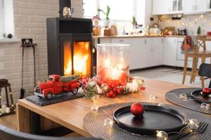 Festive interior of house is decorated for Christmas and New Year in loft style with black stove, fireplace, Christmas tree. Warm studio room with set table, burning wood, cozy and heating of home photo