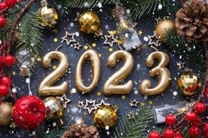 The golden figures 2023 made of candles on a black stone slate background are decorated with a festive decor of stars, sequins, fir branches, balls and garlands. Greeting card, happy New Year. photo