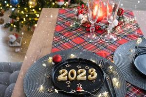 Golden figures 2023 from candles on a black plate on a festive table with a New Year's serving. Loft-style interior, party, feast. Wicker napkin, fork, knife photo