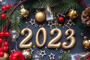 The golden figures 2023 made of candles on a black stone slate background are decorated with a festive decor of stars, sequins, fir branches, balls and garlands. Greeting card, happy New Year. photo