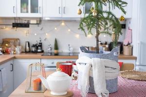 Festive Christmas decor in white kitchen, festive breakfast, white scandi interior. Araucaria as a Christmas tree is decorated and wrapped in a scarf and felt planters. New Year, mood, cozy home