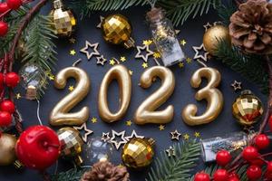 The golden figures 2023 made of candles on a black stone slate background are decorated with a festive decor of stars, sequins, fir branches, balls and garlands. Greeting card, happy New Year. photo