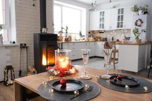 el interior festivo de la casa está decorado para navidad y año nuevo en estilo loft con estufa negra, chimenea, árbol de navidad. cálida sala de estudio con mesa puesta, madera quemada, acogedora y calefacción del hogar foto