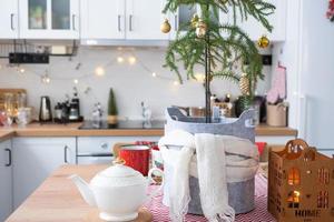 Festive Christmas decor in white kitchen, festive breakfast, white scandi interior. Araucaria as a Christmas tree is decorated and wrapped in a scarf and felt planters. New Year, mood, cozy home