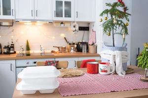 Food delivery service containers on table white scandi festive kitchen in christmas decor. Eve New year, saving time, too lazy to cook, hot order, disposable plastic box in fairy light. mock up photo