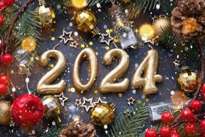 The golden figures 2024 made of candles on a black stone slate background are decorated with a festive decor of stars, sequins, fir branches, balls and garlands. Greeting card, happy New Year. photo