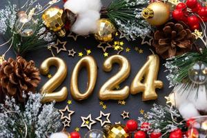 The golden figures 2024 made of candles on a black stone slate background are decorated with a festive decor of stars, sequins, fir branches, balls and garlands. Greeting card, happy New Year. photo