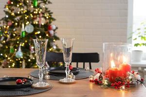 Festive table set in the living room for Christmas and New year in loft style. Christmas tree, black plates and forks, woven napkins, trendy tableware, cozy interior of the house photo