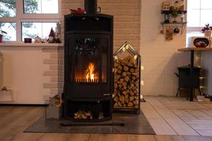 Chimenea de estufa de metal negro con madera en una pila de leña - el interior de una casa de pueblo privada. calefacción y calefacción de la casa con leña, el calor del fuego del hogar. foto